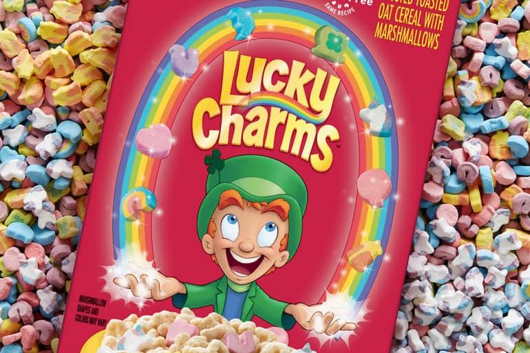 Una caja de cereal de avena de Lucky Charms Frosted Toasted con bombones rodeados de cereal Lucky Charms™.