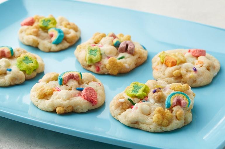 Six Magically Delicious Cereal Cookies sprinkled with Lucky Charms™ Honey Clover cereal served on a blue tray.
