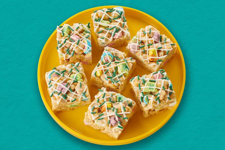 Overhead shot of 7 Lucky Charms™ Honey Clovers Cereal Bars on a round yellow plate with green background.